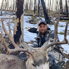 A man is sitting on the back of a deer in the woods.
