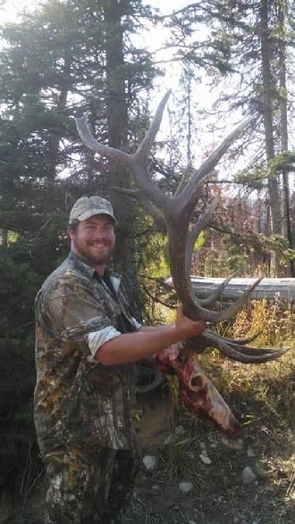 A man is holding a large deer antlers in the woods.