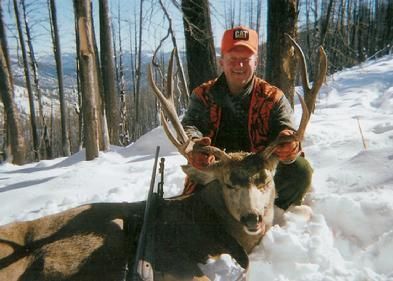 A man is kneeling next to a deer in the snow.