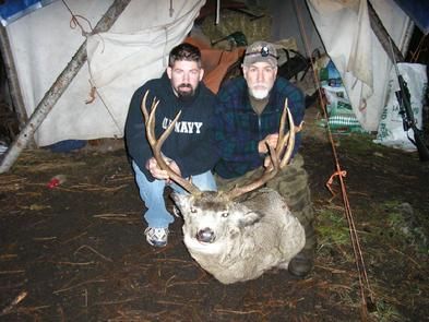 Two men standing next to a large deer with one wearing a navy shirt