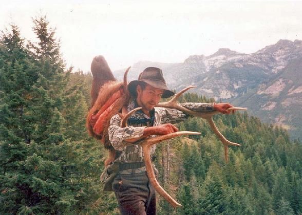 A man is carrying antlers on his back in the woods.