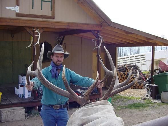 A man in a cowboy hat is holding a large deer antlers