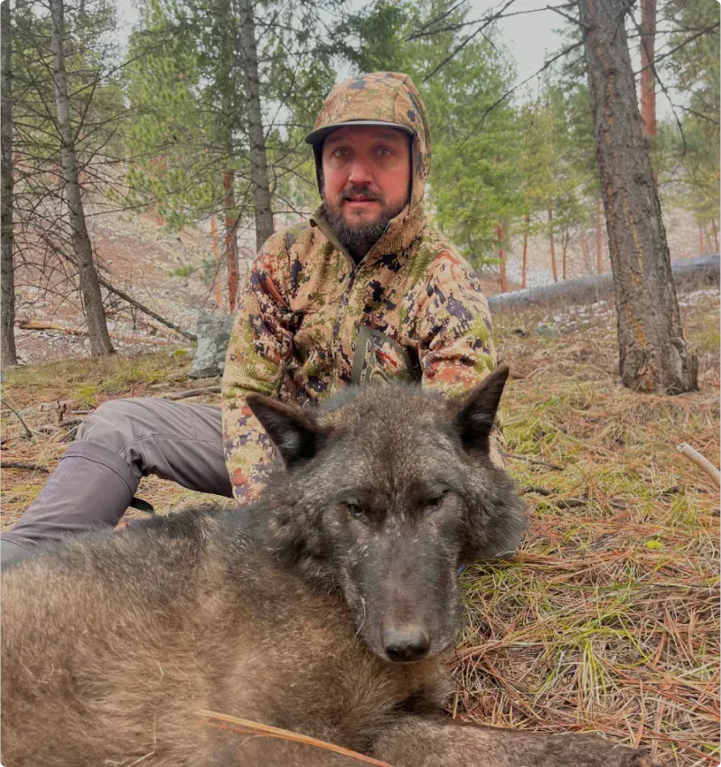 A man is sitting next to a wolf in the woods
