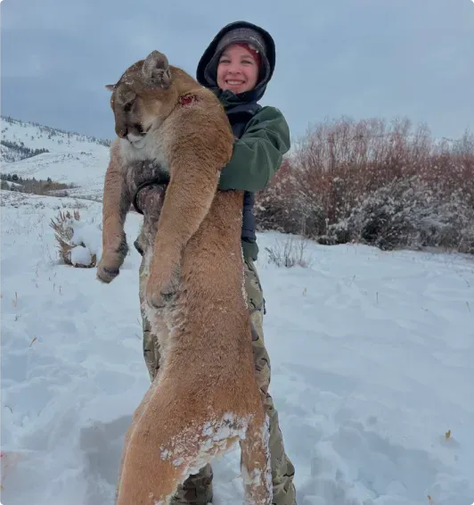 A man is holding a mountain lion in his arms in the snow