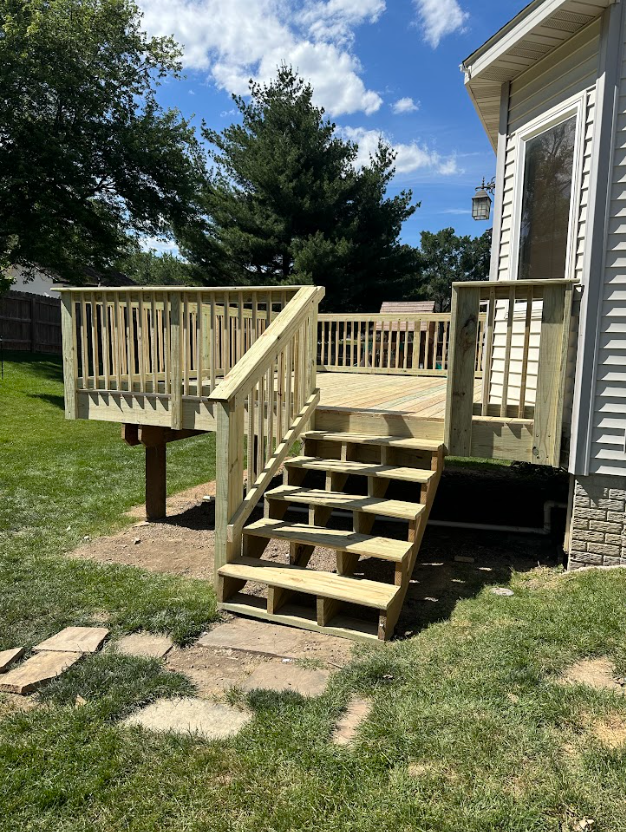 A man is kneeling down on a wooden deck with a drill and hammer.