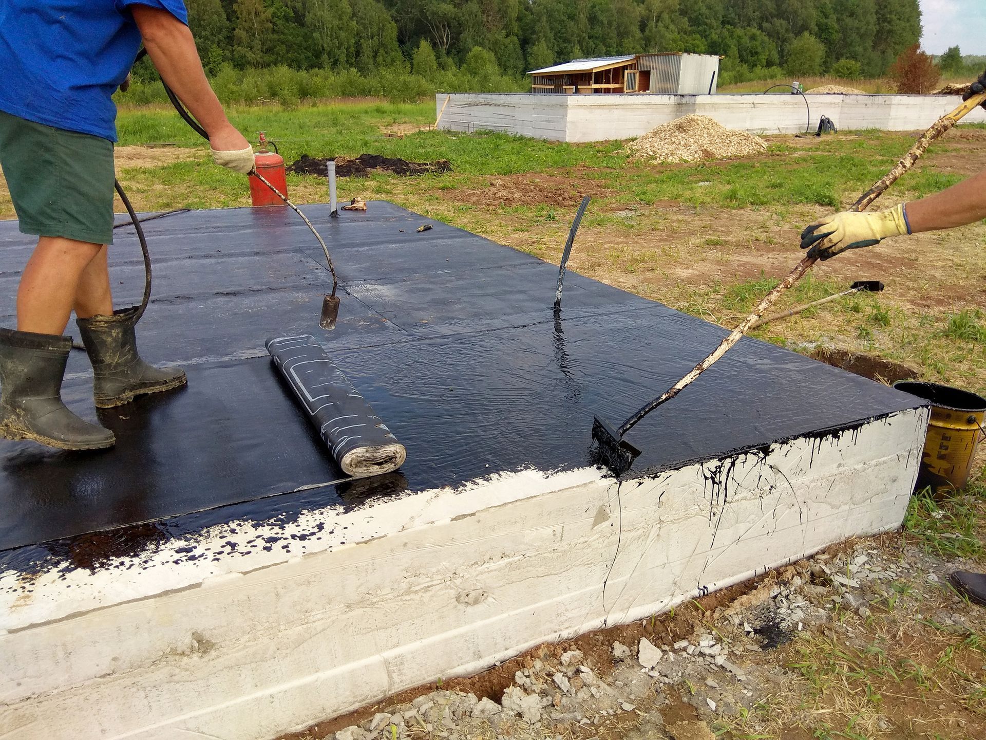 Two men are painting a concrete base with black paint.