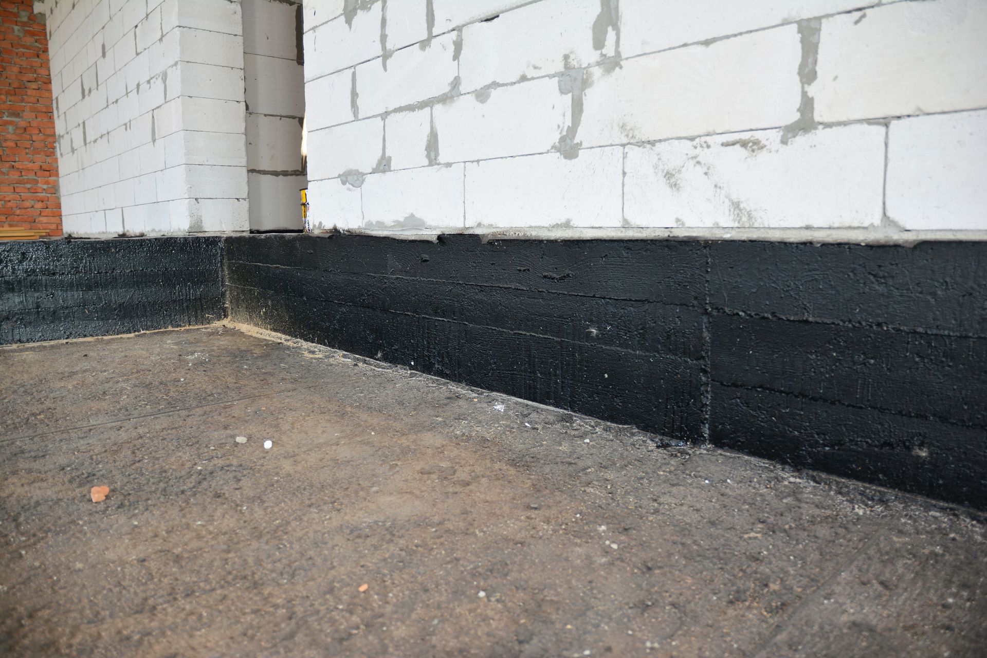 The foundation of a house is being waterproofed with black paint.