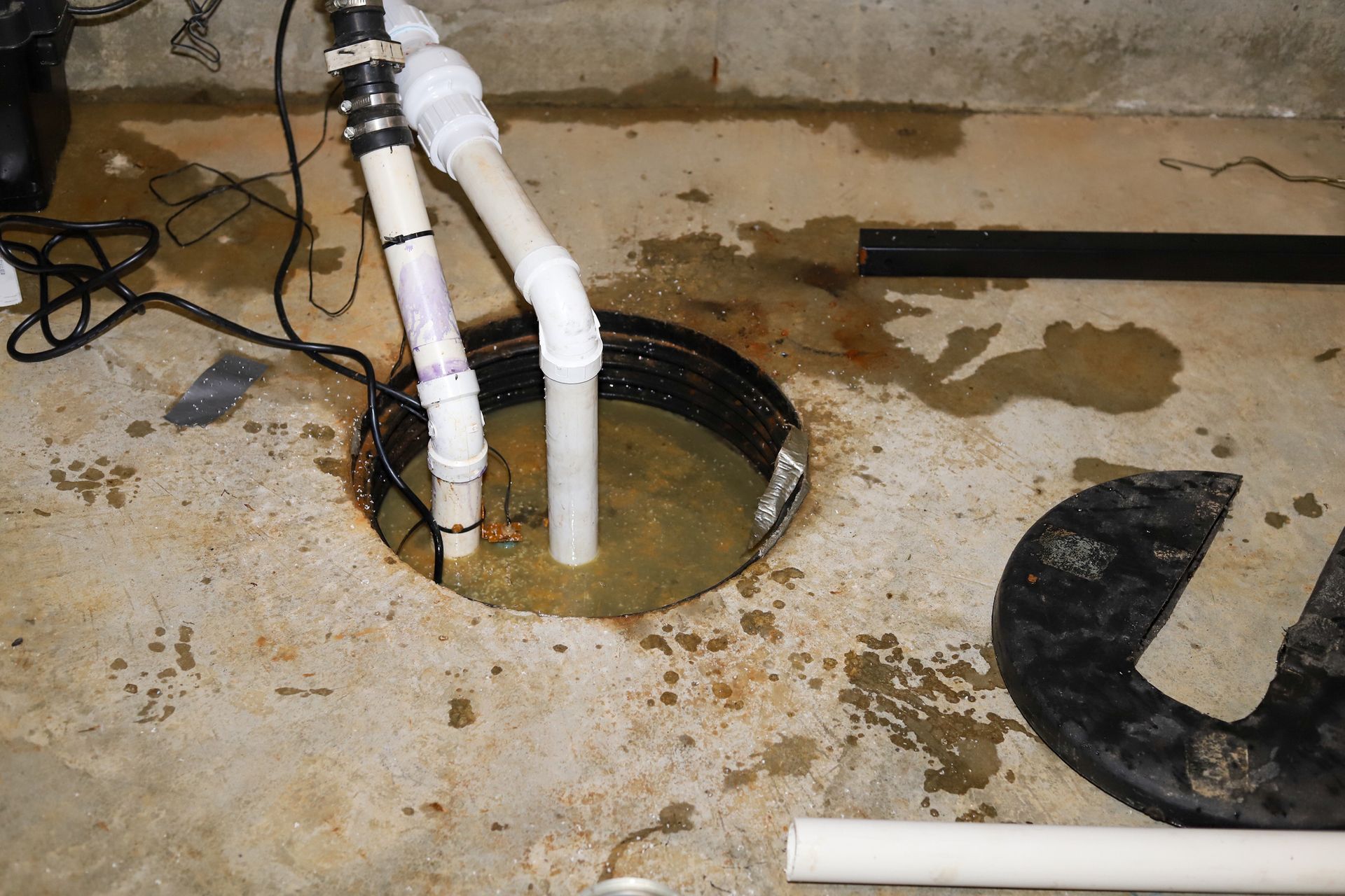 A drain in a basement filled with water and pipes.