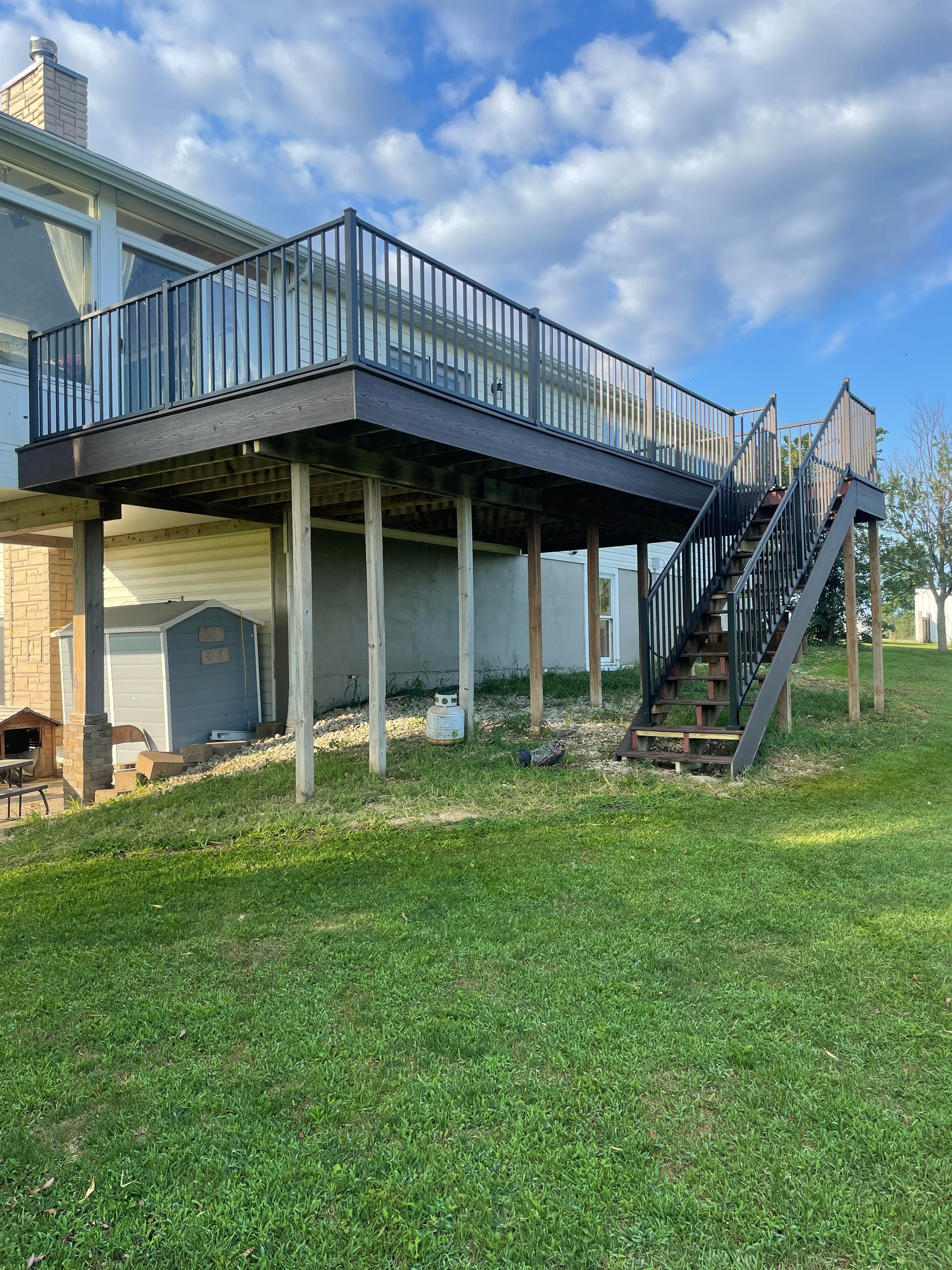 A man is kneeling down on a wooden deck with a drill and hammer.