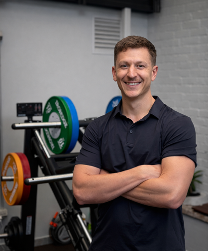 A man in a black shirt is standing in front of a barbell in a gym.