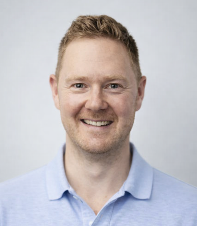 Dr Leigh Golding in a suit and tie is smiling in a black and white photo.