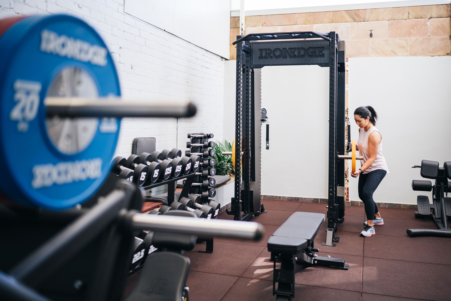 A woman is squatting in a gym with a barbell in the foreground.