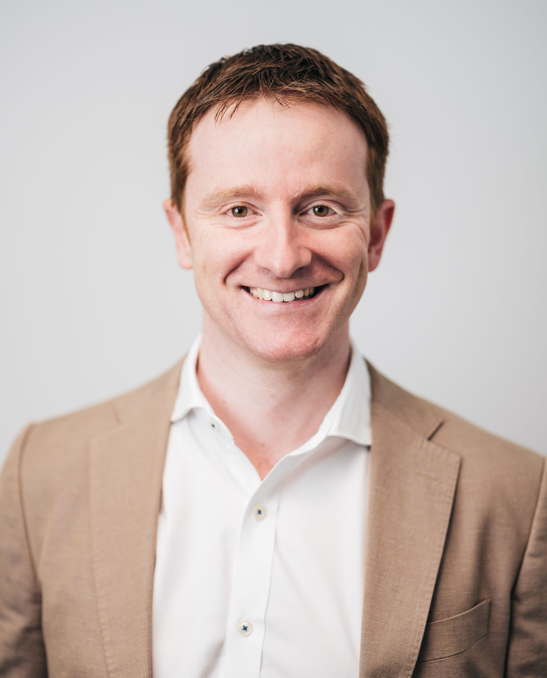 A man in a suit and white shirt is smiling for the camera.