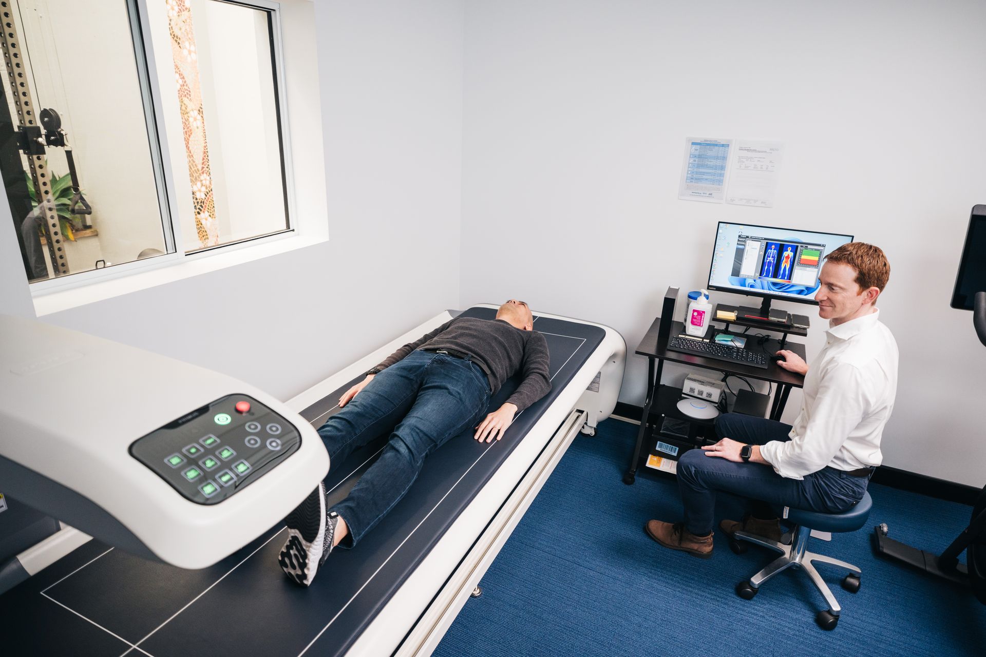 A man is sitting at a desk while a woman is laying on a bed.