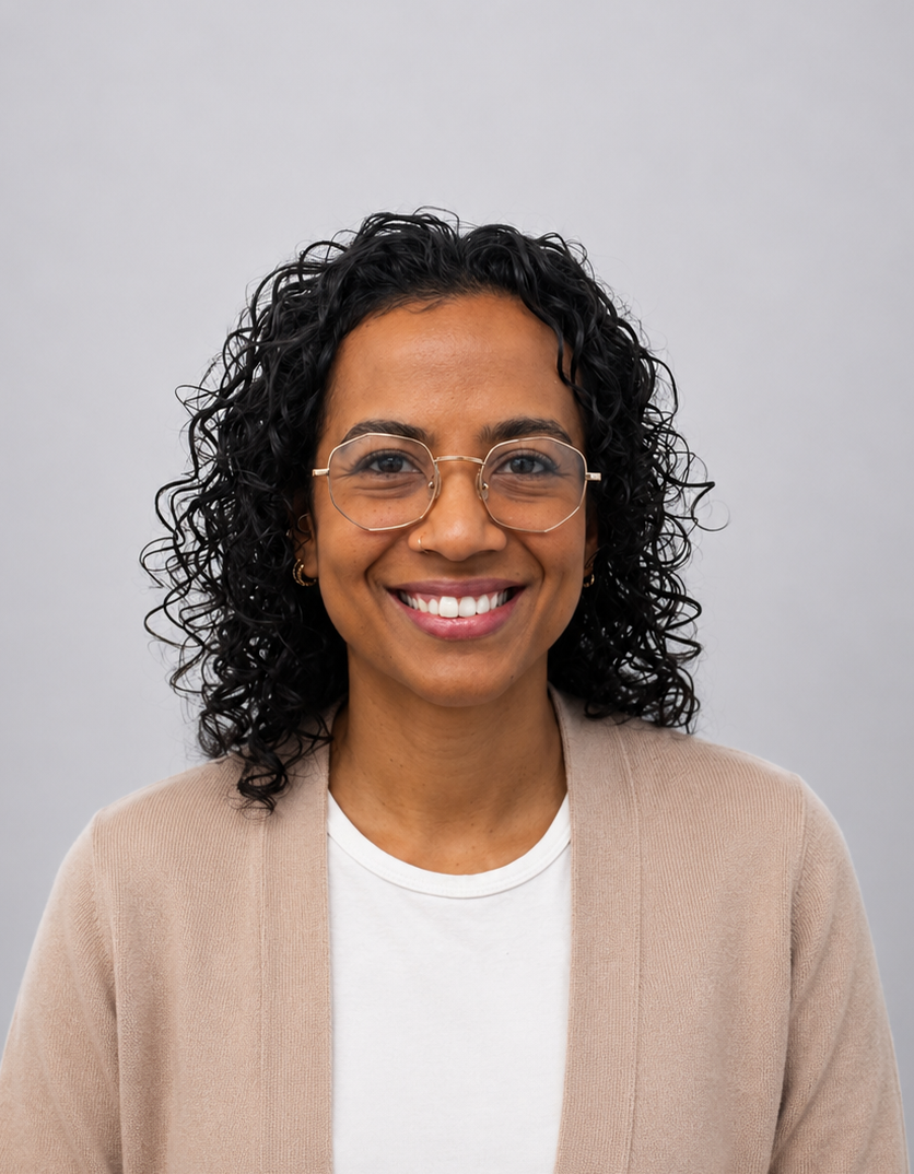 Smiling person with curly hair and glasses, wearing a beige cardigan over a white shirt. Dietitian