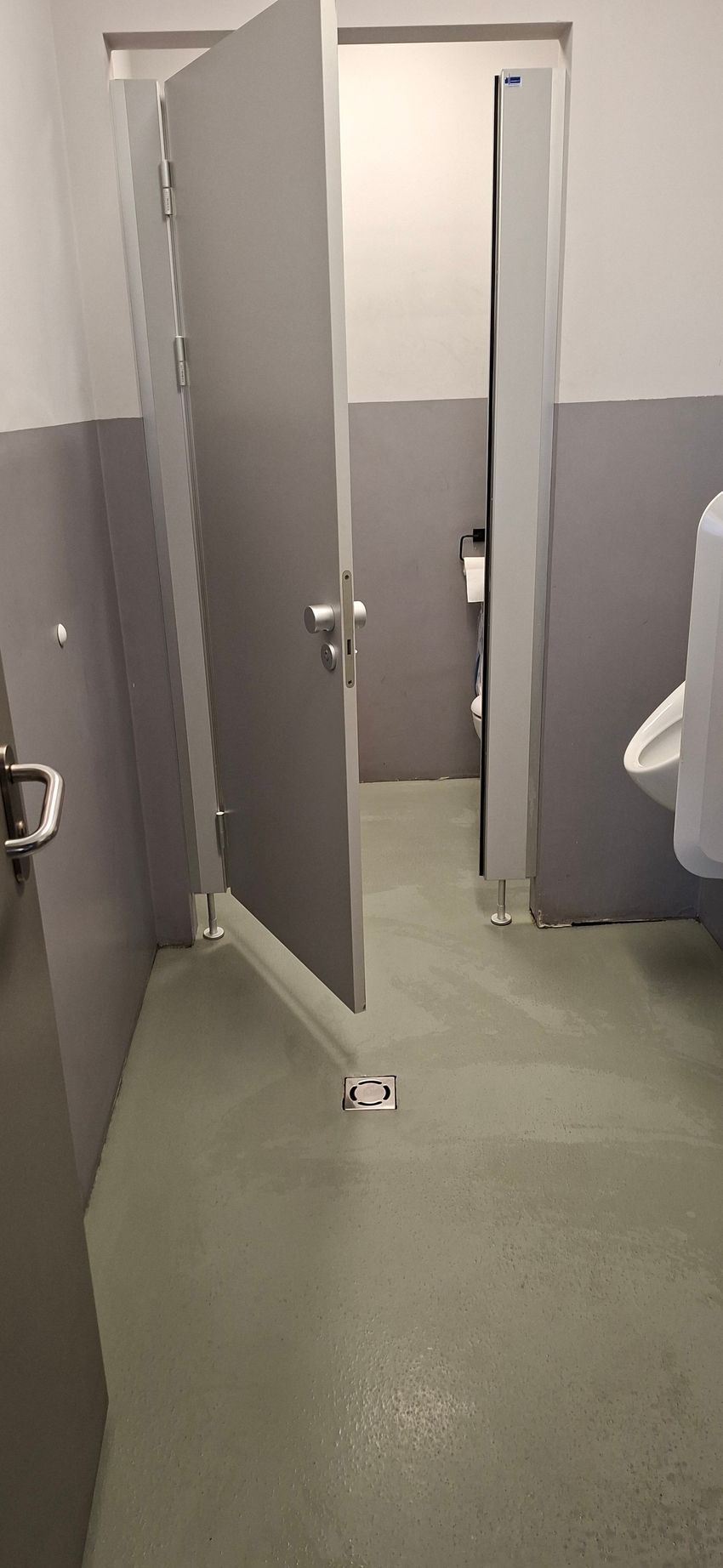 Badezimmer mit grauen Duschkabinentüren, eine davon angelehnt. Hellgrüner Boden.