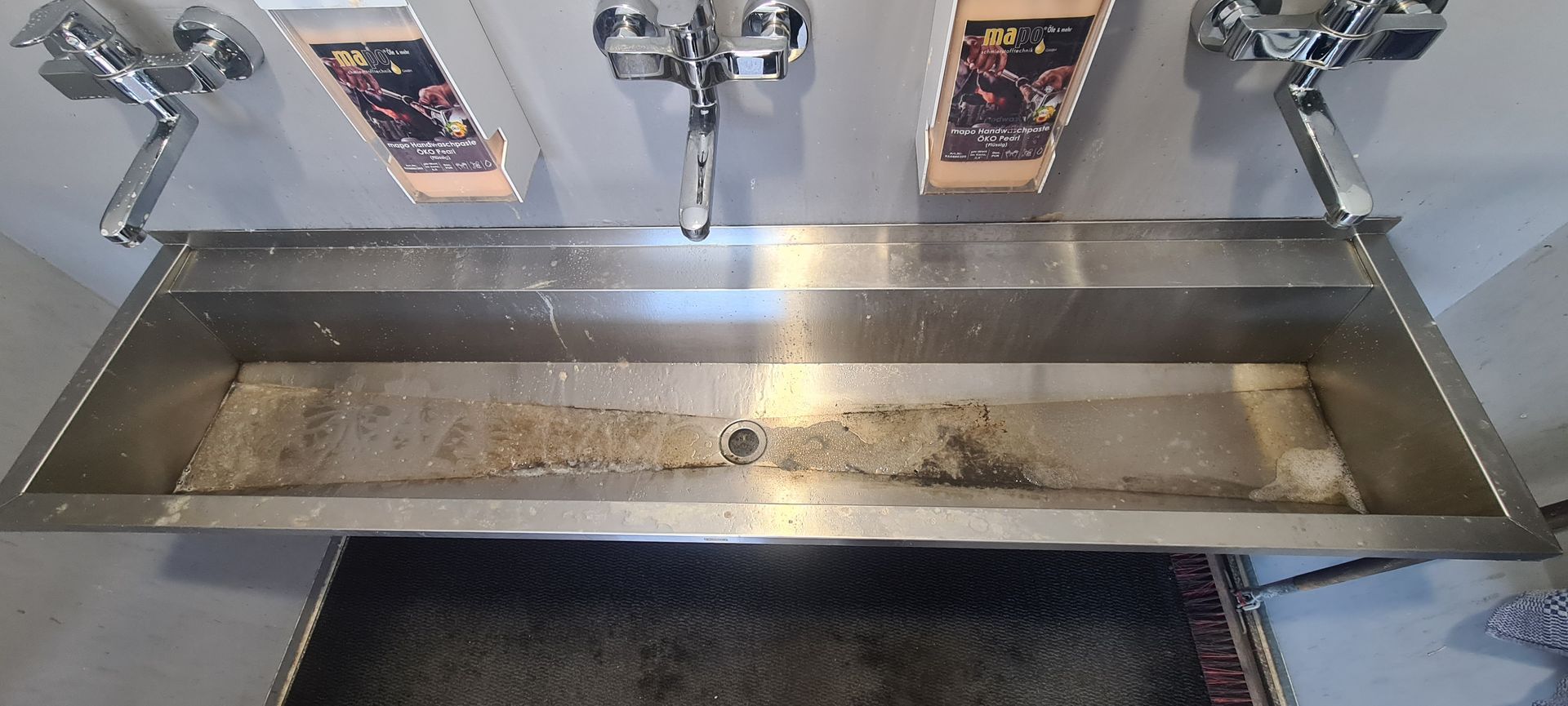 Edelstahlspüle mit drei Wasserhähnen, auf der eine Schale mit Speiseresten steht