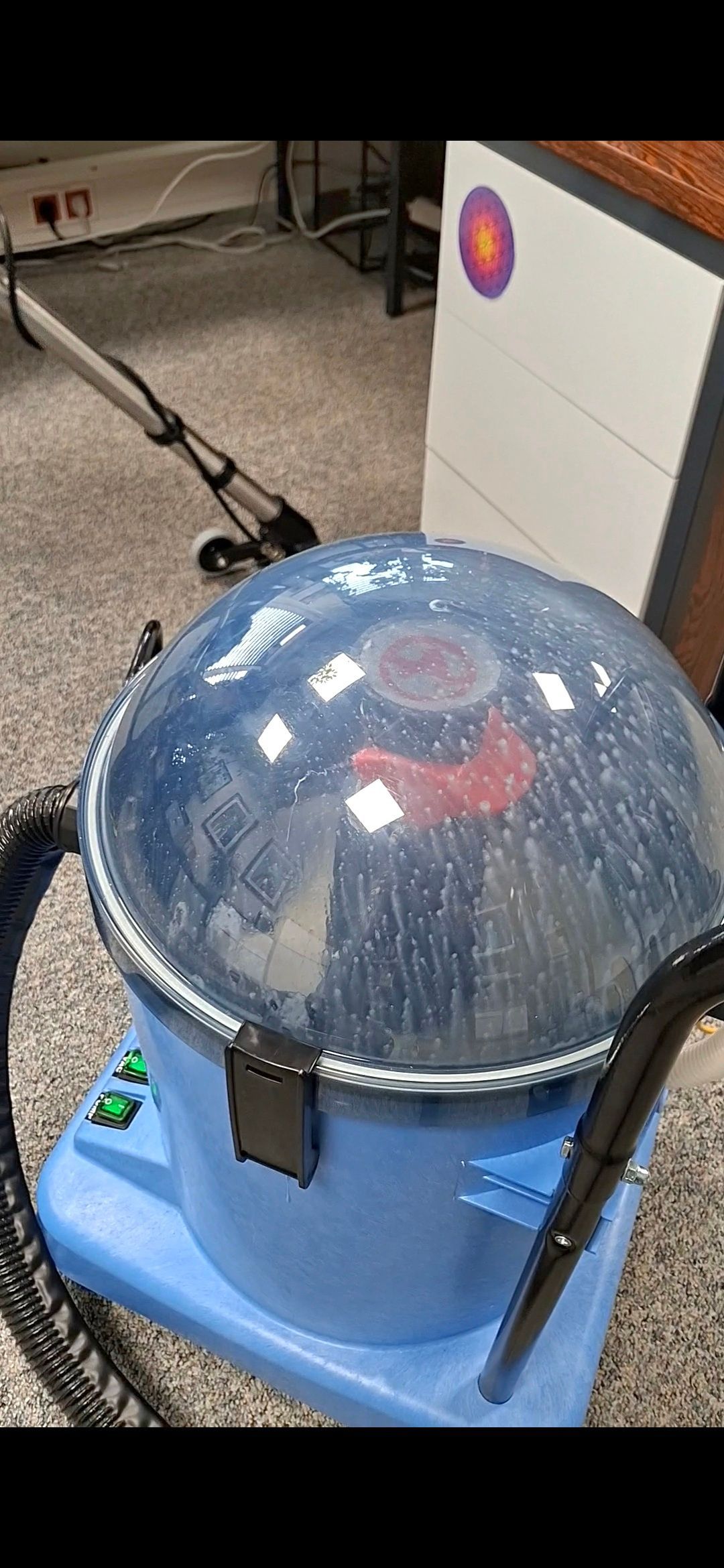 Industrieller Teppichreiniger in Blau und Silber auf einem Betonboden mit angeschlossenem Schlauch und Griff.