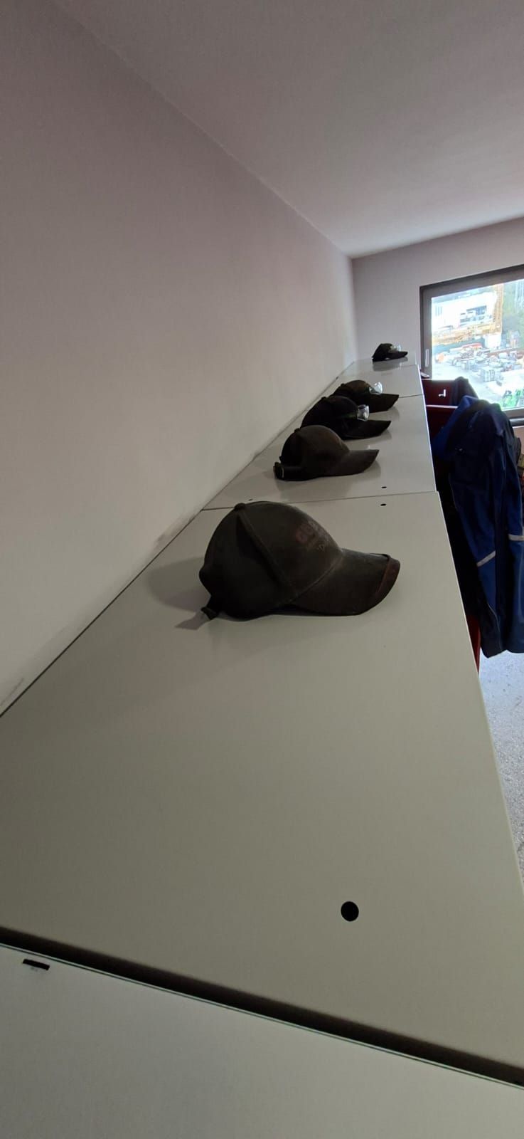 Eine Reihe dunkel gefärbter Kappen, die auf einem langen, hell gefärbten Regal an einer Wand platziert sind.