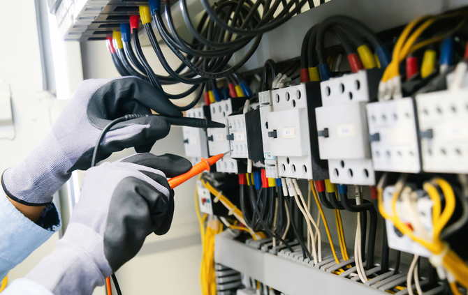 An electrician is working on an electrical panel with a screwdriver.