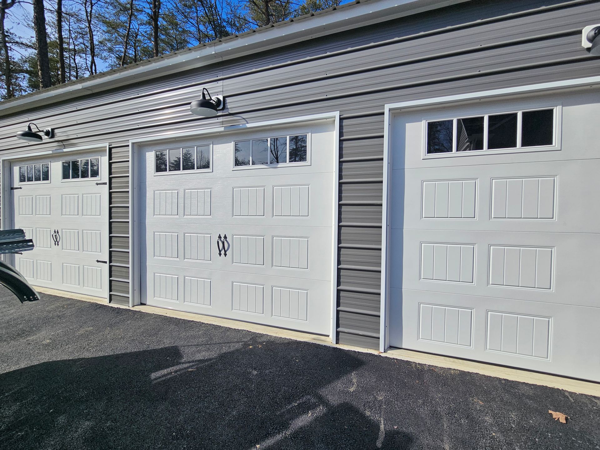 A car is parked in front of a garage with three white garage doors.
