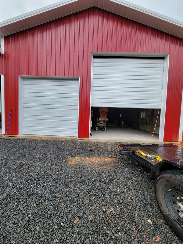 A red barn with a white garage door and a trailer parked in front of it.