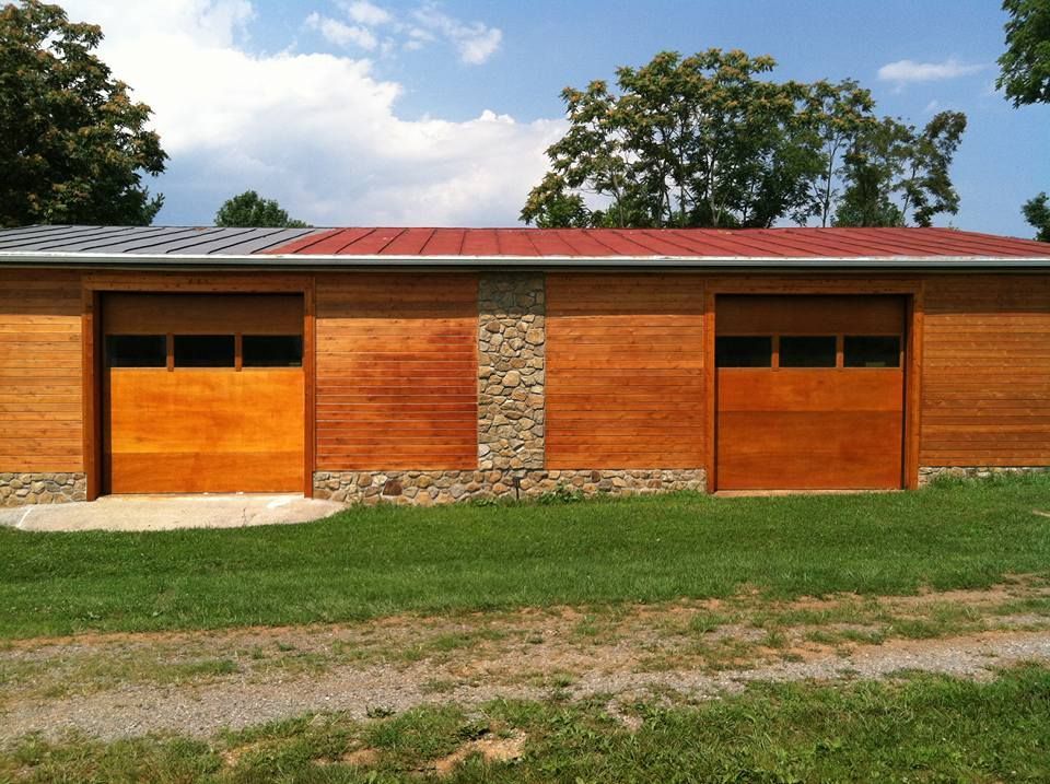 A large wooden garage with two wooden garage doors and a red roof.