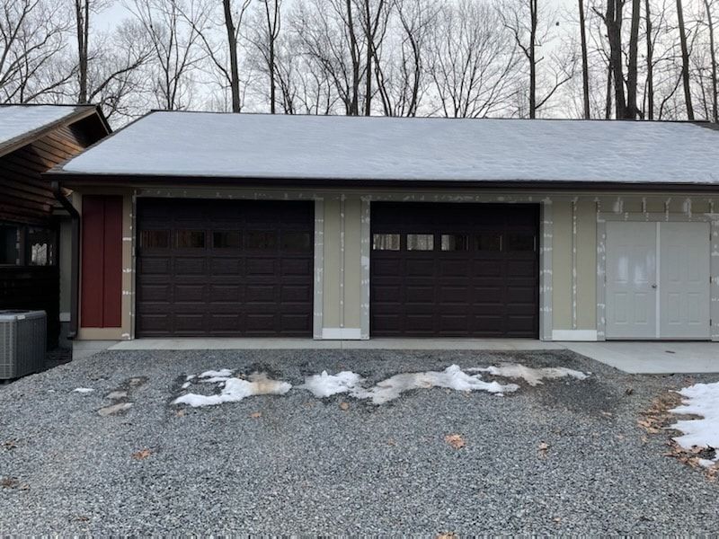 A garage with two garage doors is sitting on top of a gravel driveway.
