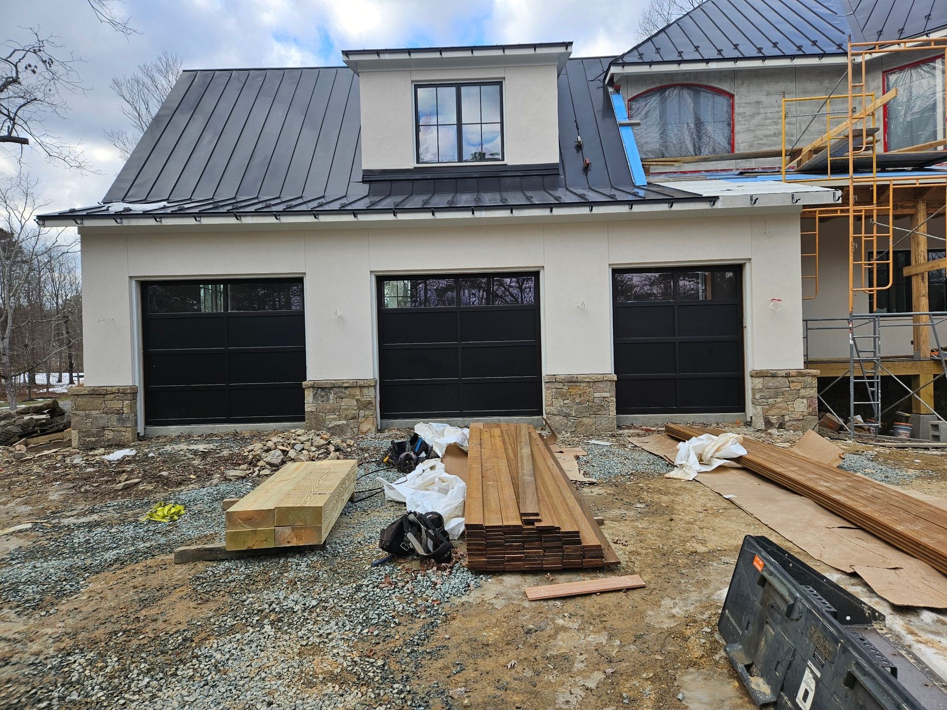 A house is being built with black garage doors and a metal roof.