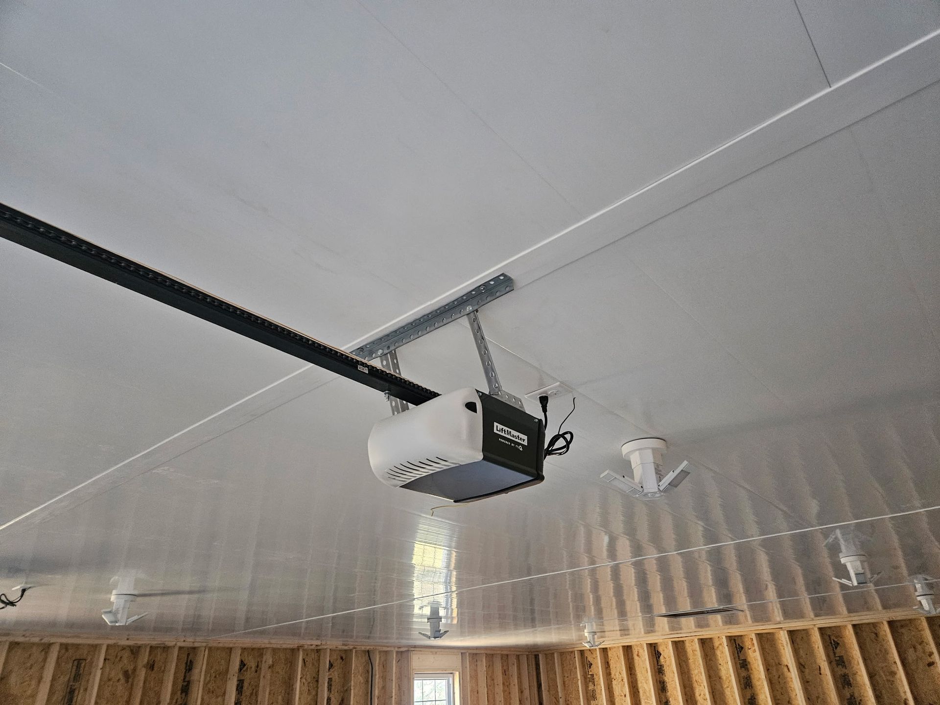 A garage door opener is hanging from the ceiling of a garage under construction.