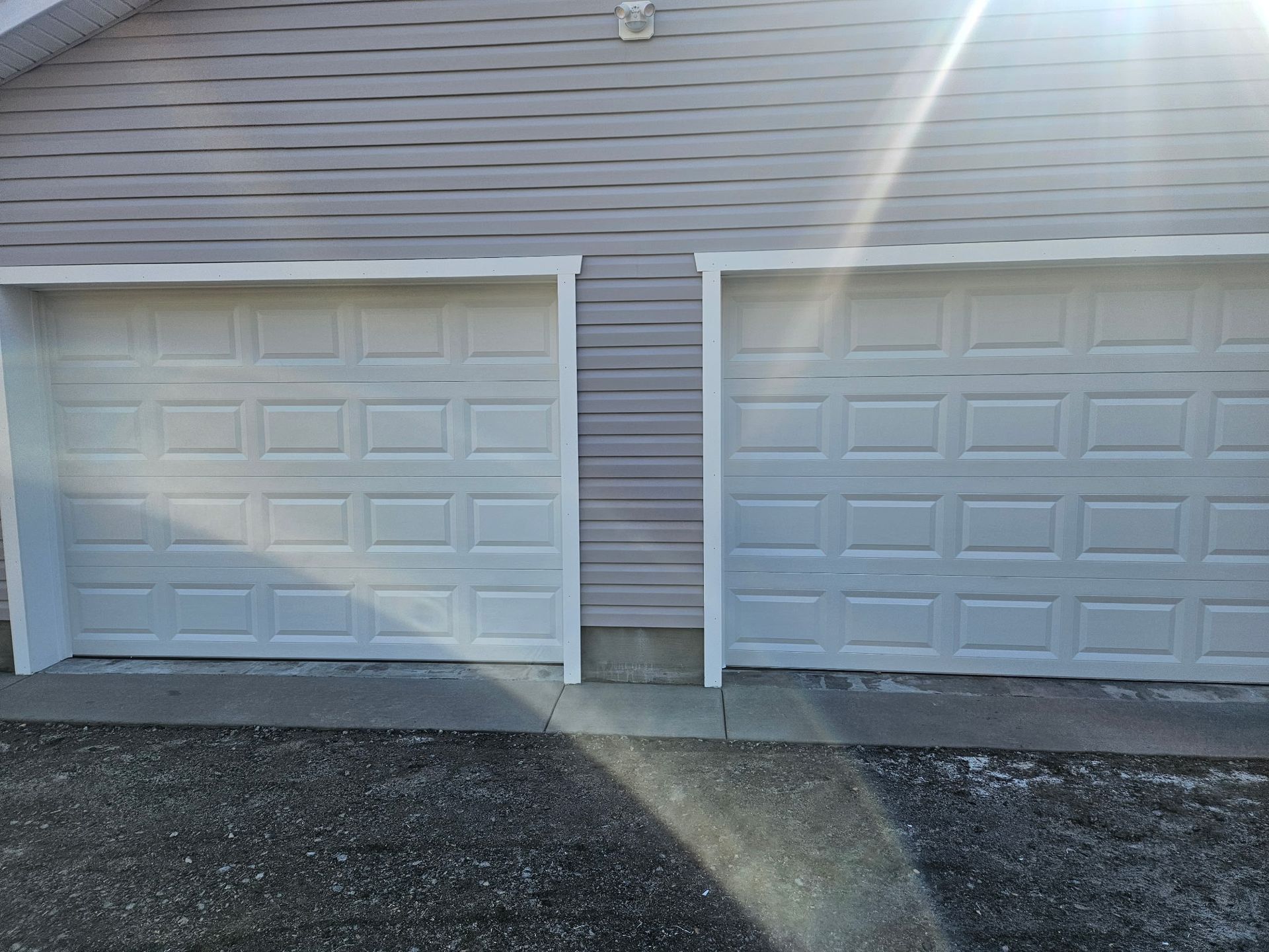 Two white garage doors are sitting next to each other on the side of a house.