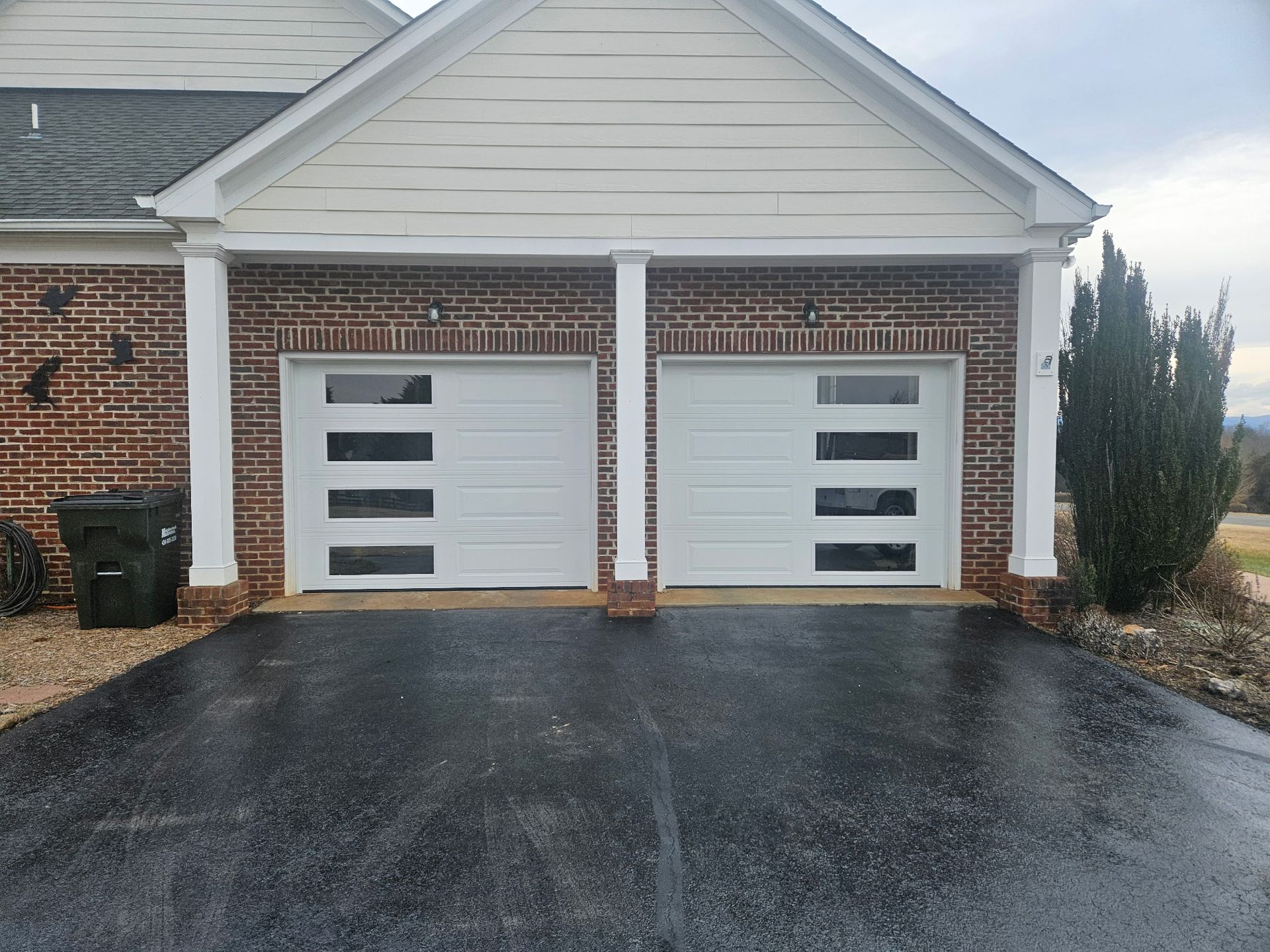 A brick house with two white garage doors and a black driveway.