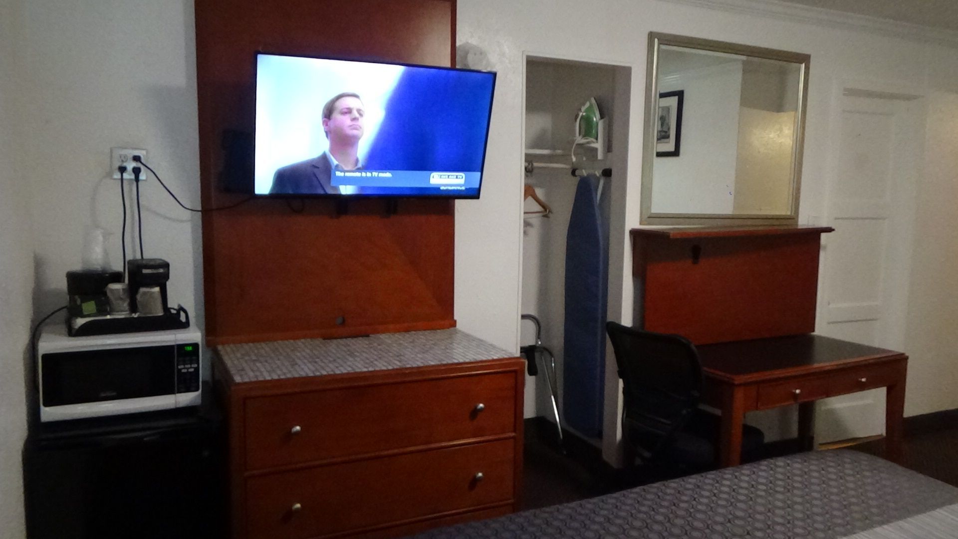 Hotel room interior with TV, dresser, microwave, desk, ironing board, mirror, and bed.