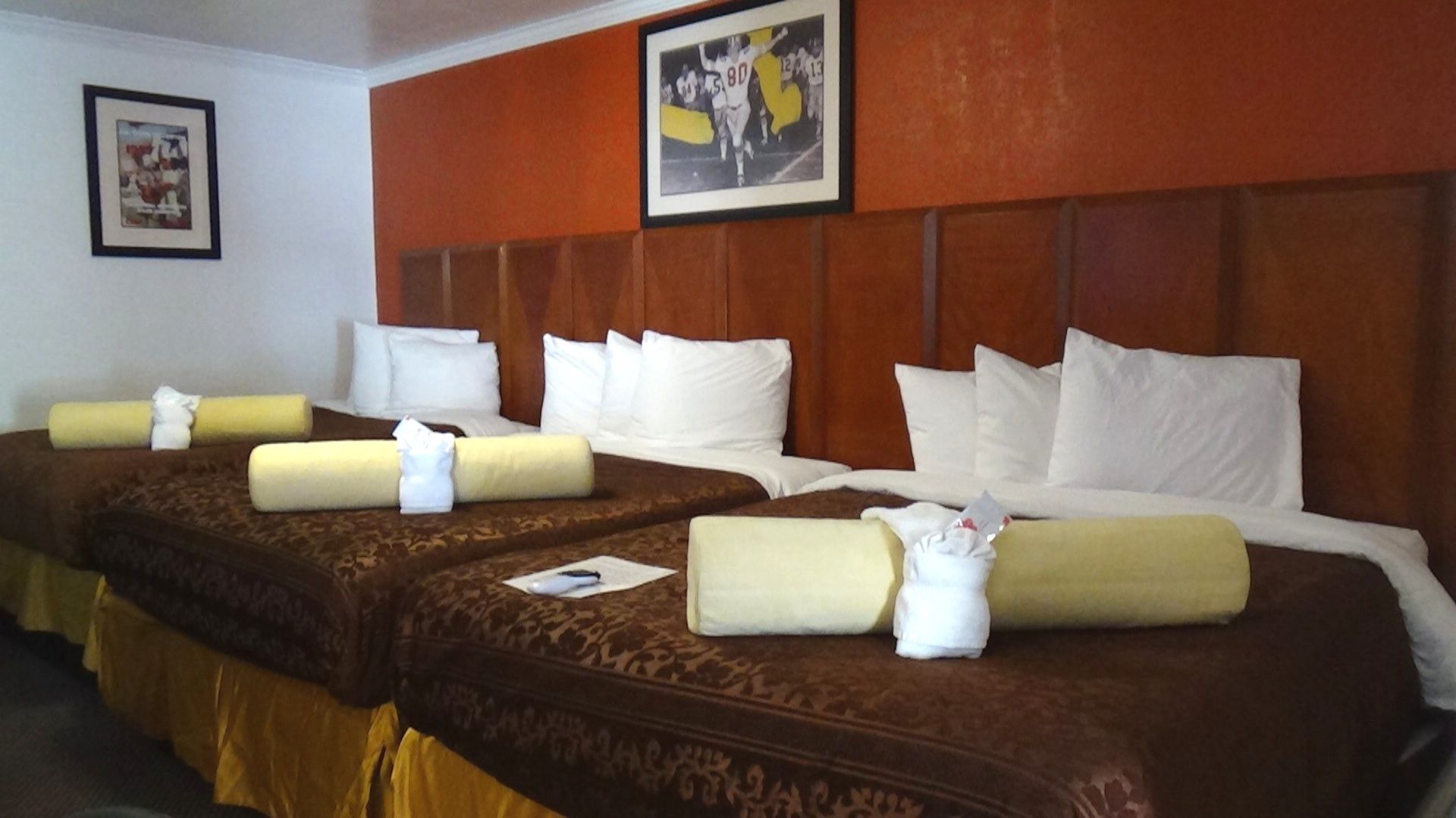 Hotel room with three double beds, dark wood headboards, and orange accent wall.