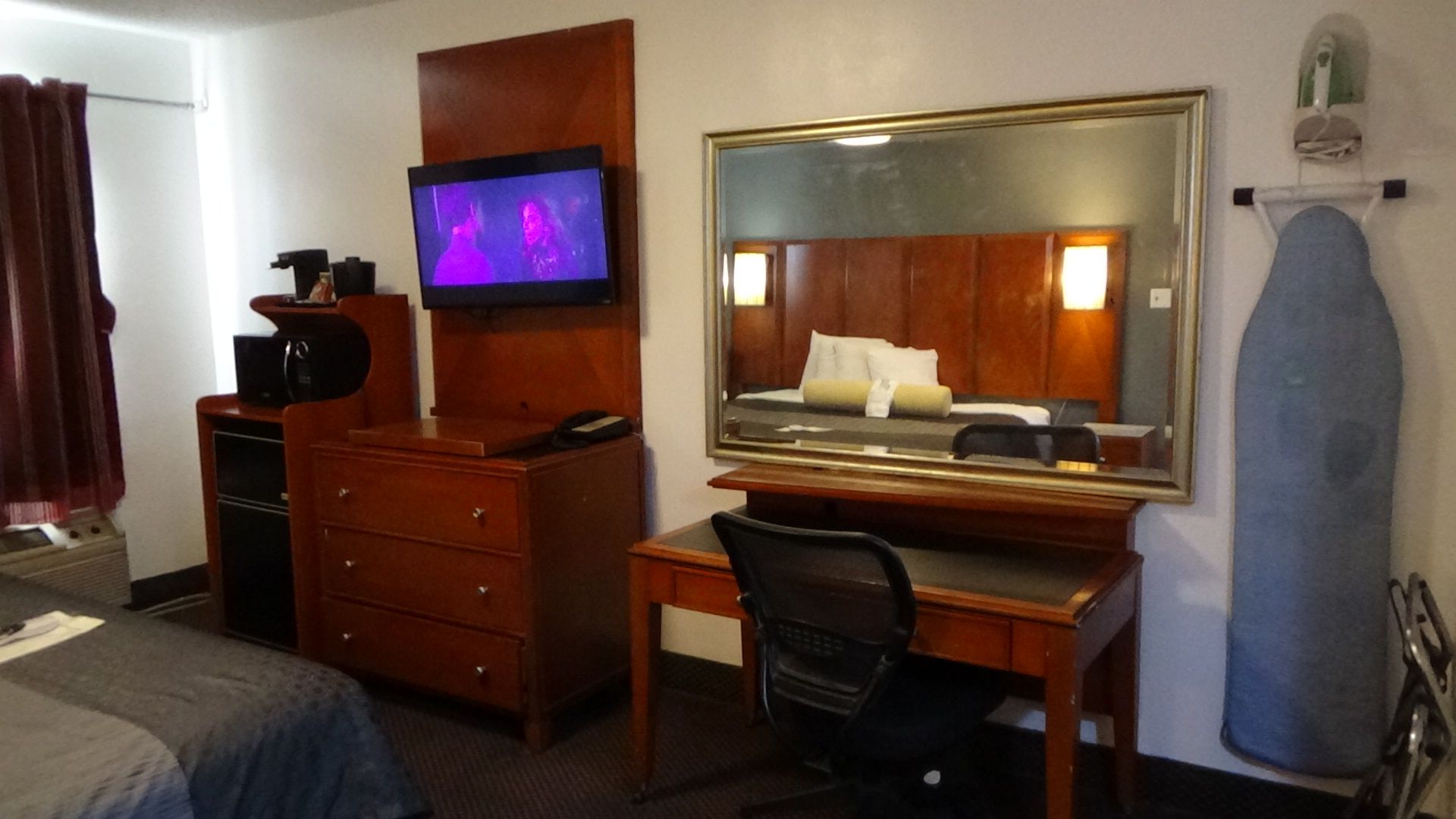 Hotel room interior with bed, desk, dresser, TV, and ironing board.