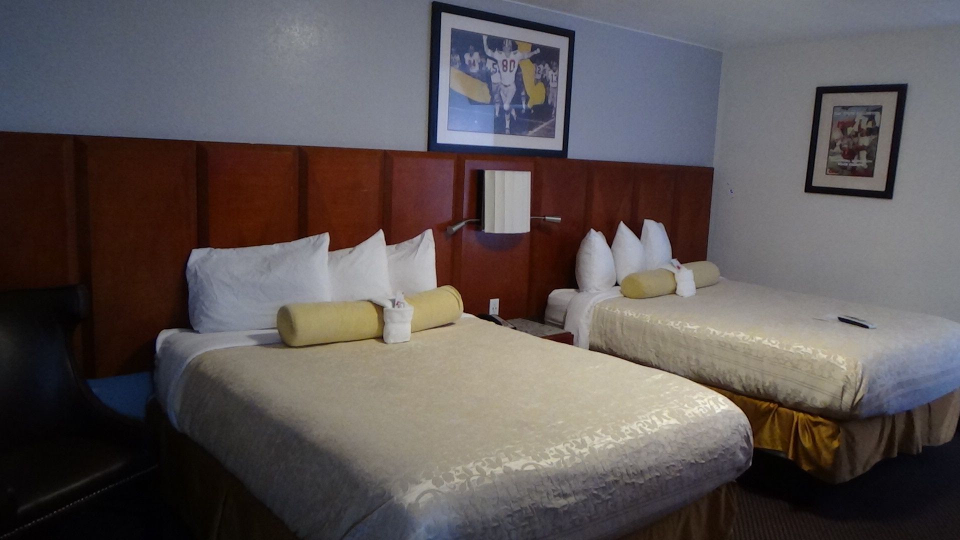 Hotel room with two beds, brown headboard, framed art, and light-colored bedding.