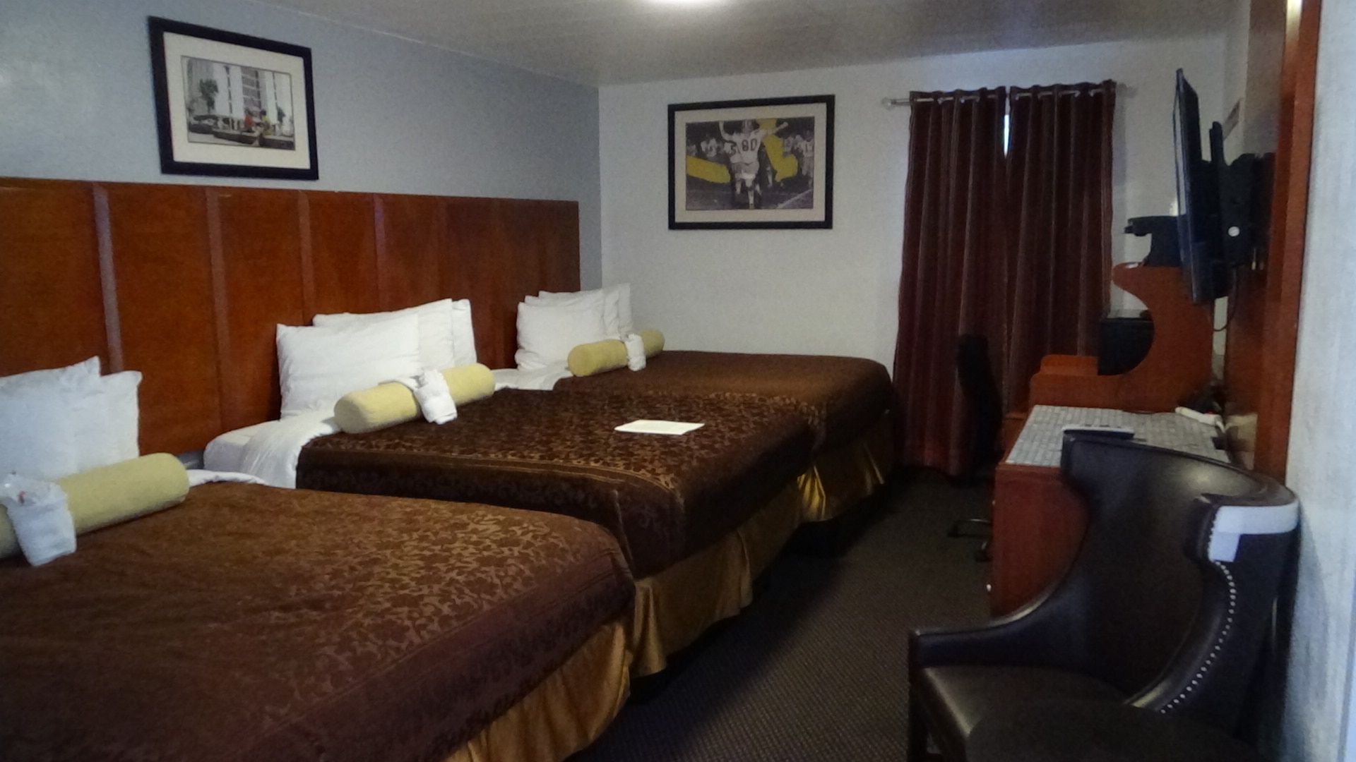 Hotel room with two double beds, brown bedding, dark wood headboard, and artwork on the walls.