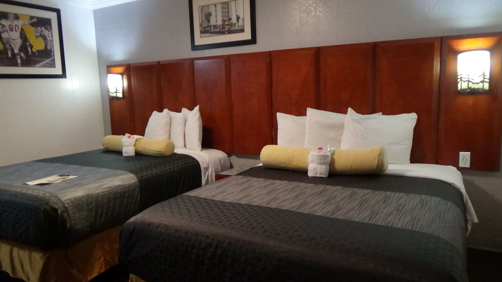 Two hotel beds with gray and black comforters, a large wood headboard, and bedside sconces.