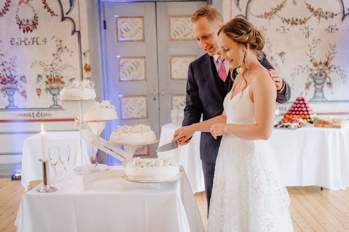 Brudeparet skjærer bryllupskake i mottakelsen, dekorert rom med veggmalerier.