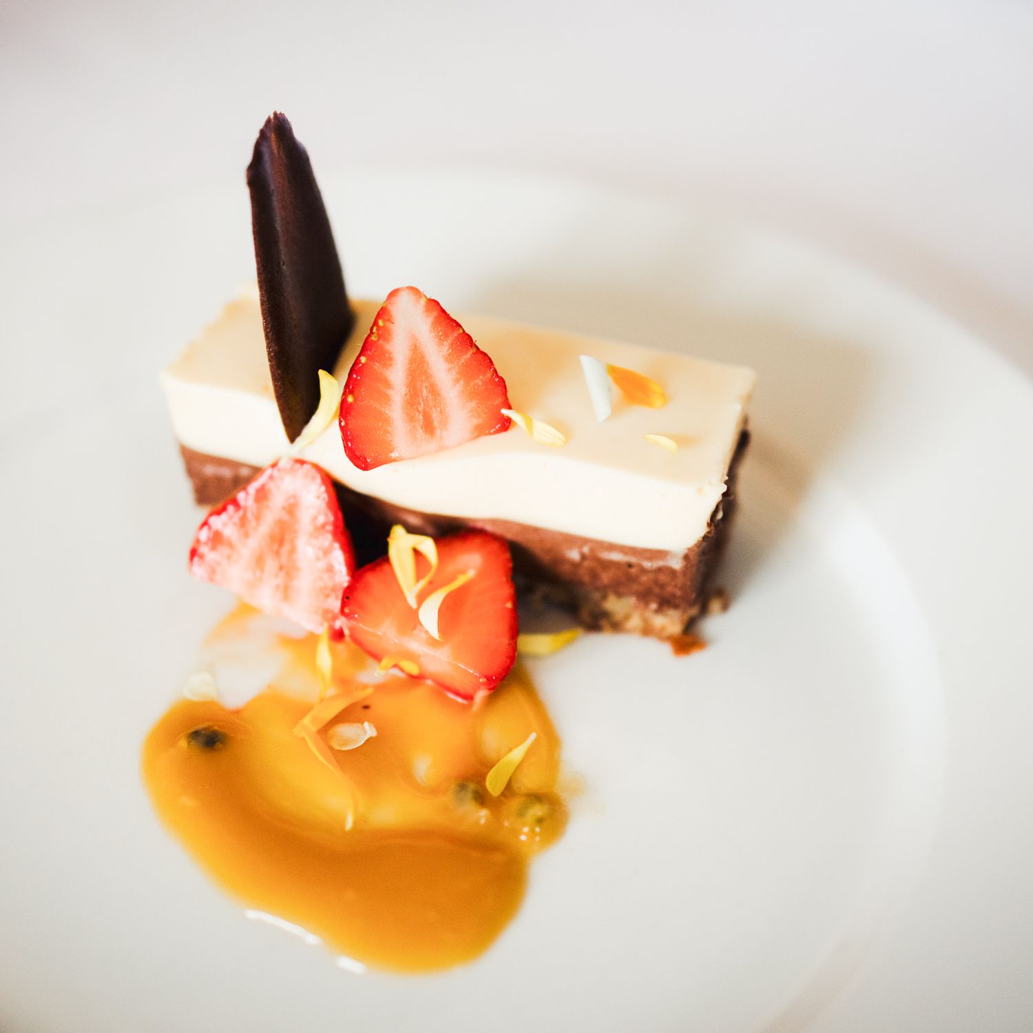 Dessert: lagdelt sjokoladekake med jordbær, saus og sjokoladepynt på en hvit tallerken.