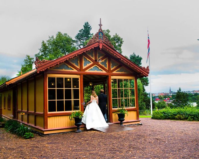 Par går inn i en dekorativ trebygning med glassvinduer, sannsynligvis for en bryllupsseremoni.