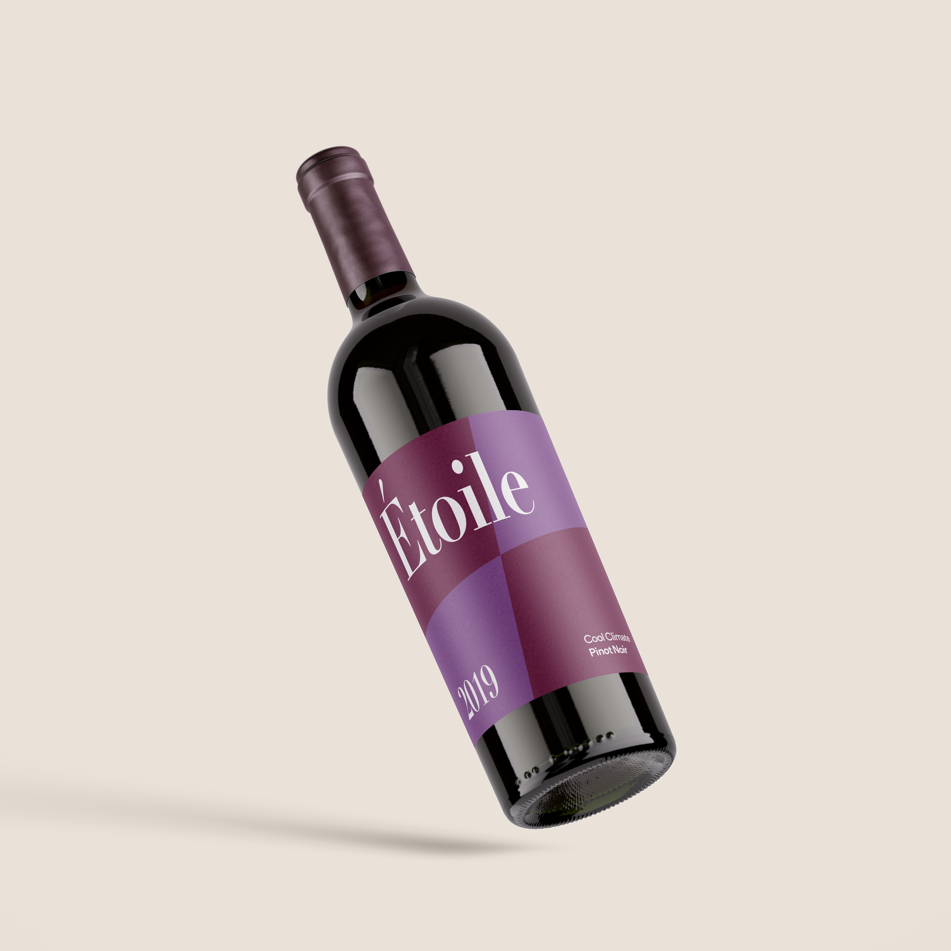Flaske Étoile-vin, lilla og rødbrun etikett. Vinflasken står lent mot en nøytral bakgrunn.
