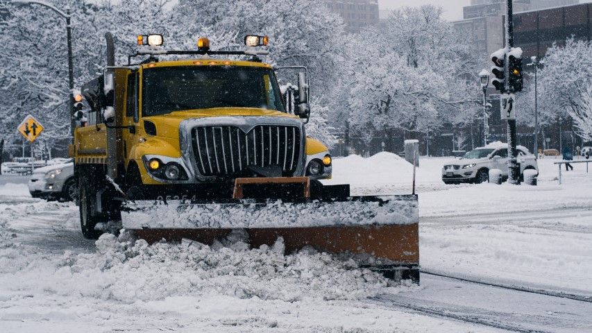 A yellow snowplow clearing snow from a city street during a winter storm.