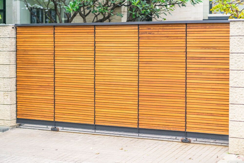 Wooden Slat Driveway Gate Between Beige Stone Columns — Trade Fencing Supplies in Moolap, VIC