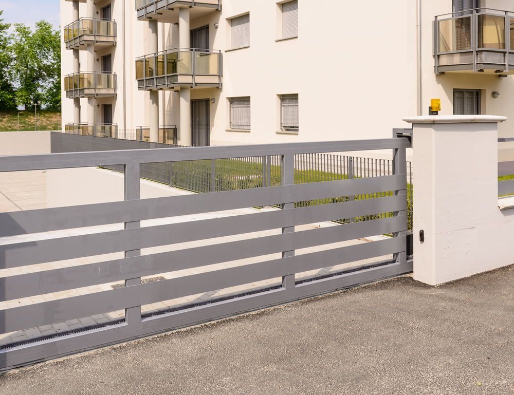 Grey Sliding Gate in Front of a White Building With Balconies — Trade Fencing Supplies in Surf Coast, VIC