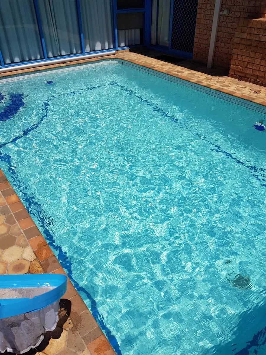 A Large Swimming Pool Filled With Blue Water in Front of a House — Cessnock Pool Shop in Cessnock, NSW