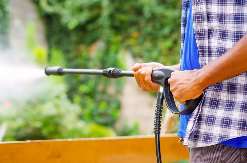 A man is holding a high pressure washer in his hands.