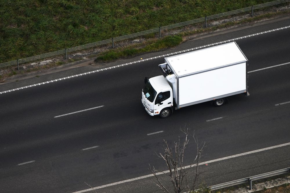 Aerial view of a white cold storage delivery truck on a highway, showcasing transportation and distribution.