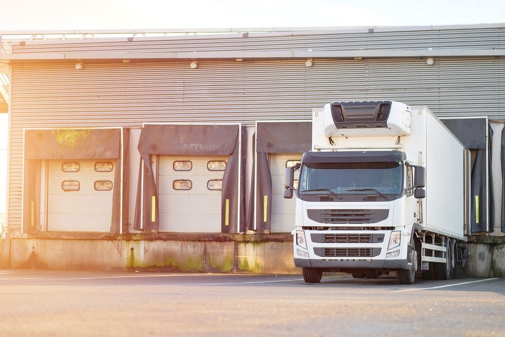 White semi-truck parked at warehouse loading docks in warm sunlight