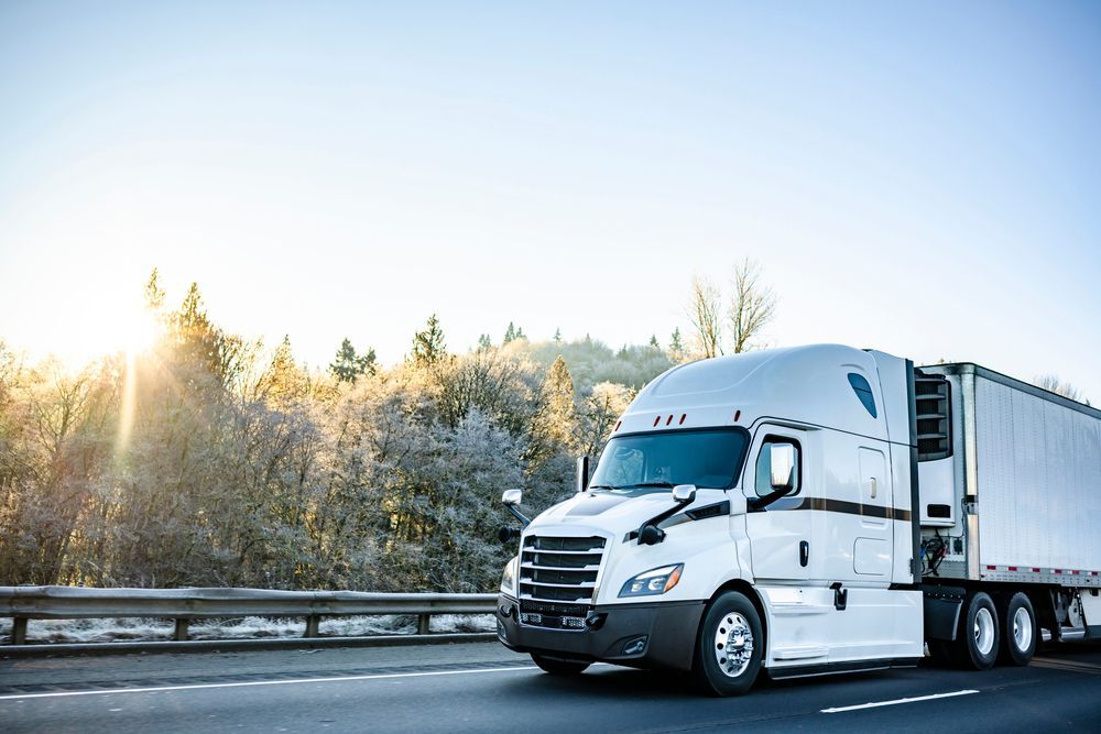 White refrigerated semi truck hauling frozen goods on snowy winter highway with frosted trees.
